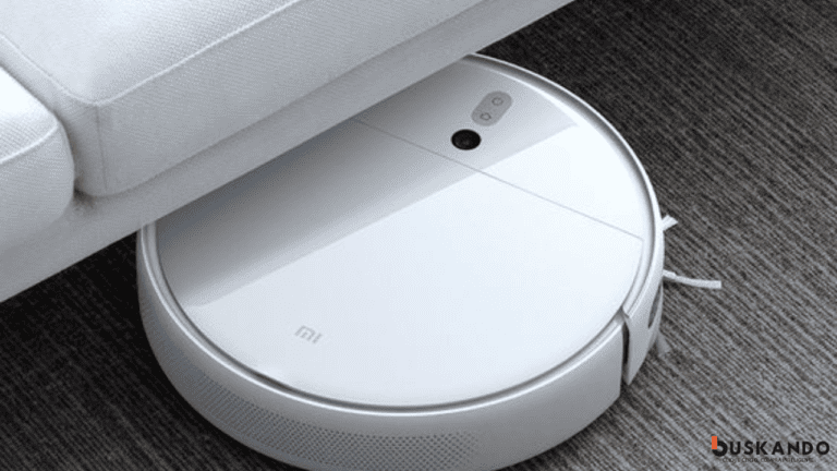 Robô aspirador de pó inteligente da marca Xiaomi navegando sob um sofá cinza, demonstrando sua capacidade de limpeza em espaços apertados.