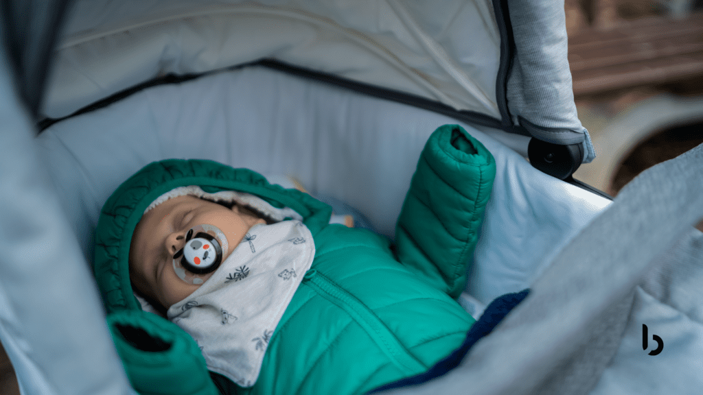 Imagem de um bebê dormindo em um carrinho de bebê, vestido com um casaco verde e chupeta, destacando a tranquilidade e o conforto proporcionados pelo carrinho.